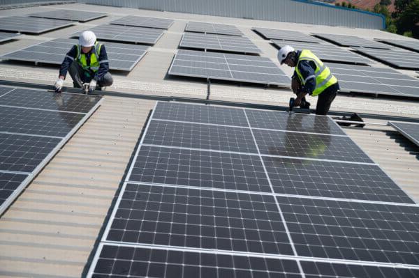 Engineers wearing high vis and hard hats working on solar panels fixed to a roof